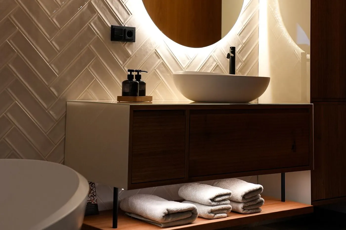 Waschtisch mit Aufsatzbecken, beleuchtetem Rundspiegel und freistehender Badewanne