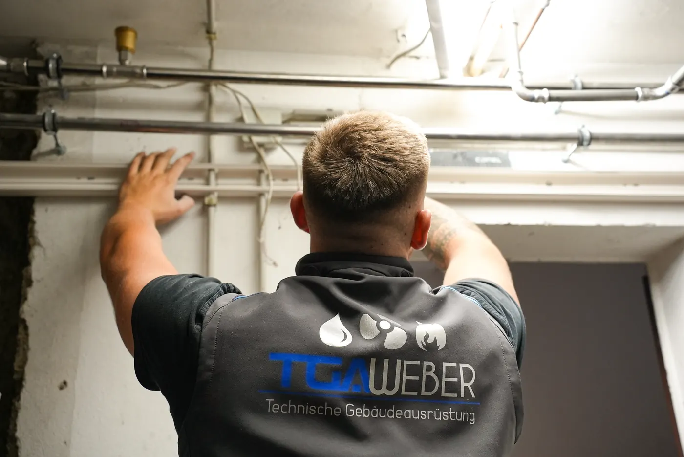 Monteur von TGA Weber bei der Arbeit an Rohrleitungen unter der Kellerdecke